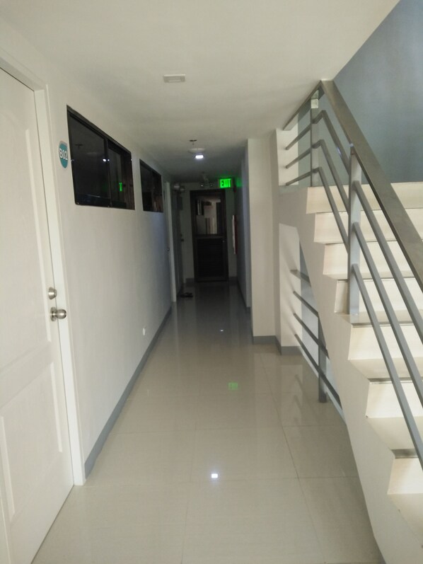 A clean, modern hallway with a staircase on the right, a door on the left, and an exit sign above the door.