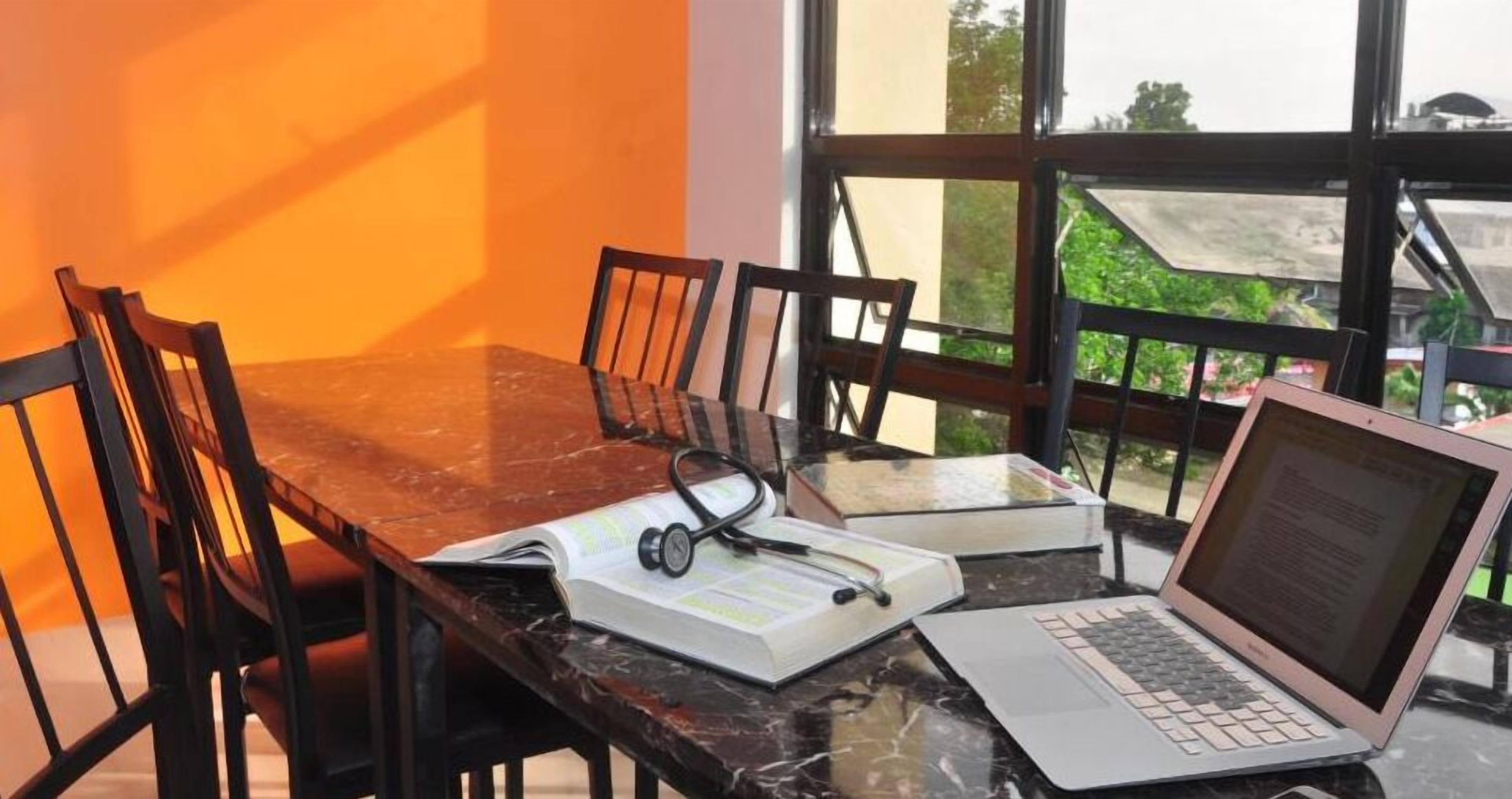 A dining table with chairs, a laptop, a book, and a stethoscope.