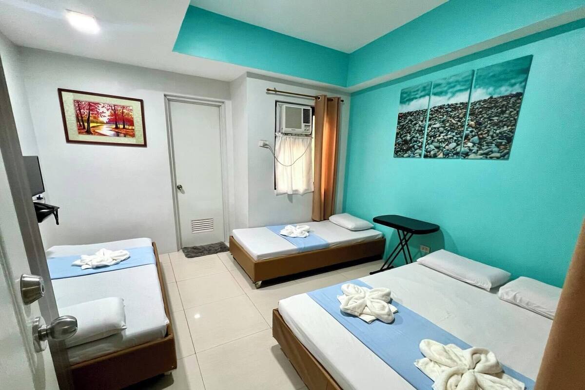 A hotel room with two beds, a small table, a window with curtains, and a painting on the wall.