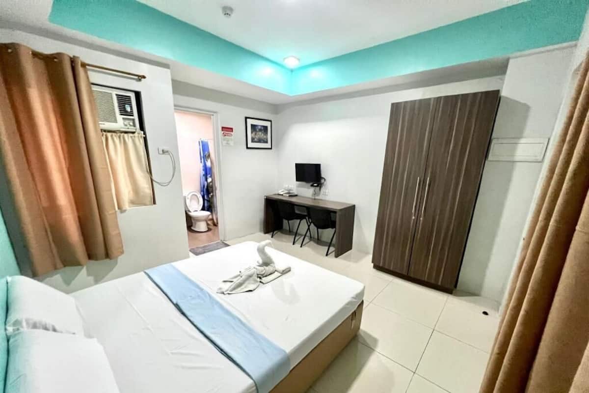 A hotel room with a bed, a desk, a wardrobe, and an air conditioning unit.