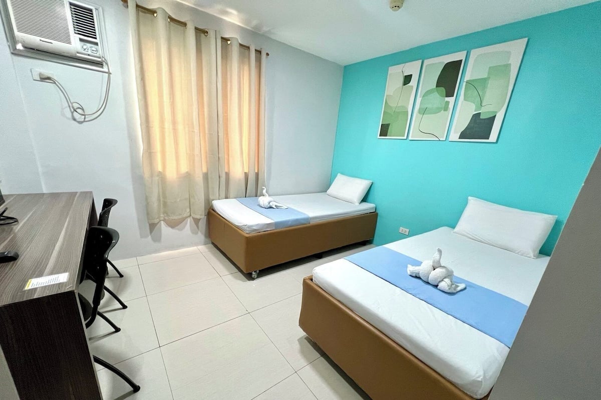 A hotel room with two beds, a desk, and a window with curtains.