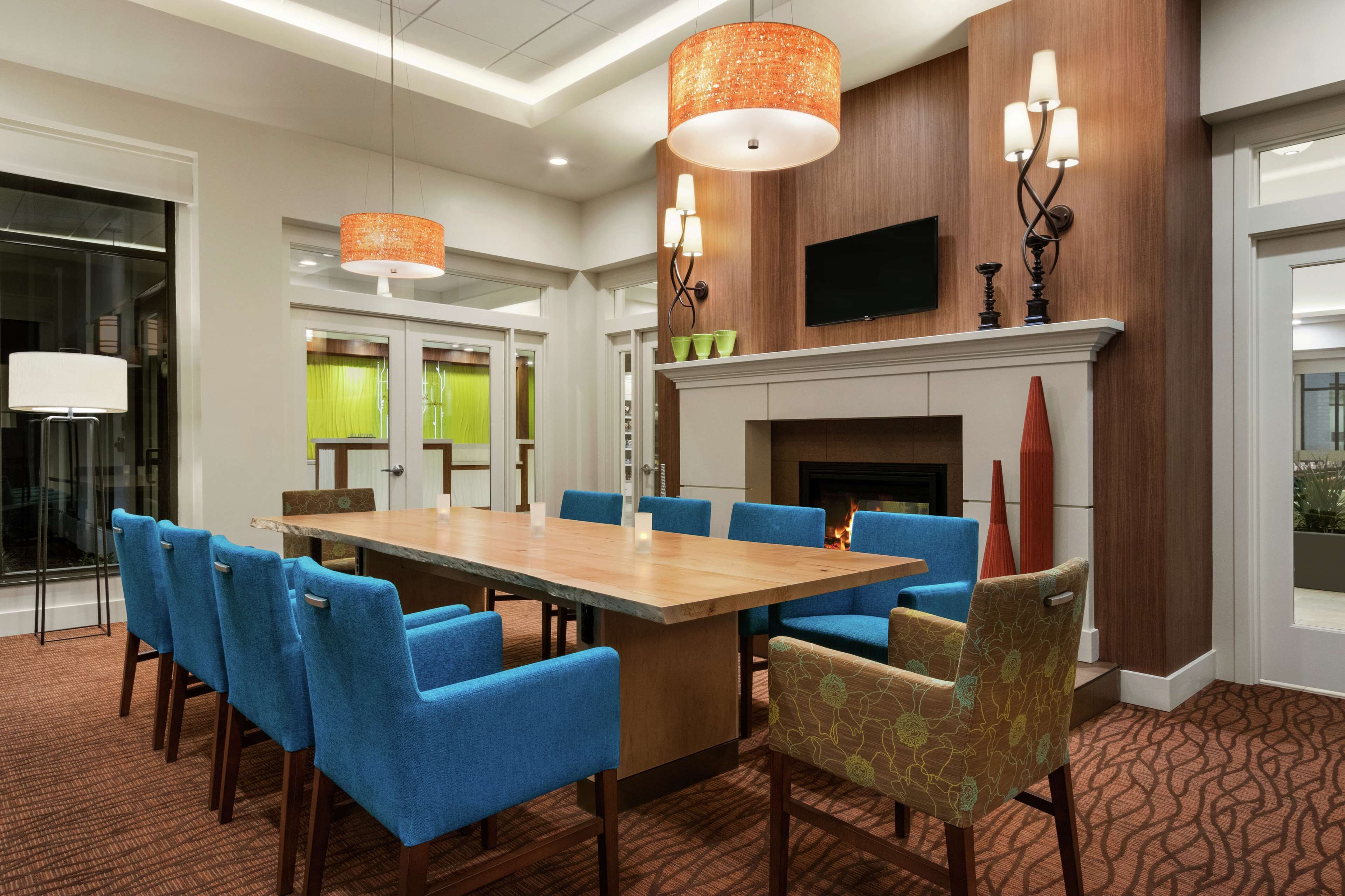 A conference room with a long table, blue chairs, a fireplace, and a television mounted on the wall.