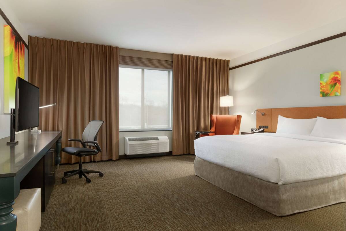 Ein Hotelzimmer mit Bett, Schreibtisch, Stuhl und einem großen Fenster mit Vorhängen.