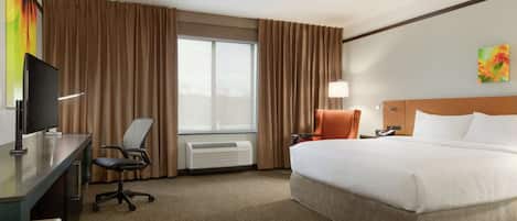 A hotel room with a bed, desk, chair, and a large window with curtains.