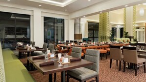 A spacious hotel dining area with multiple tables and chairs, large windows, and a modern interior design. - Hilton Garden Inn Medford, OR  (Medford)