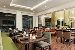 Un comedor de hotel amplio con múltiples mesas y sillas, ventanas grandes y un diseño interior moderno.