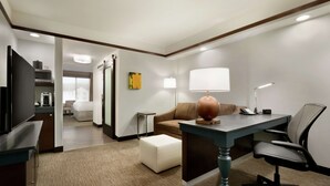 A hotel room with a desk, chair, television, and a sofa. - Hilton Garden Inn Medford, OR  (Medford)