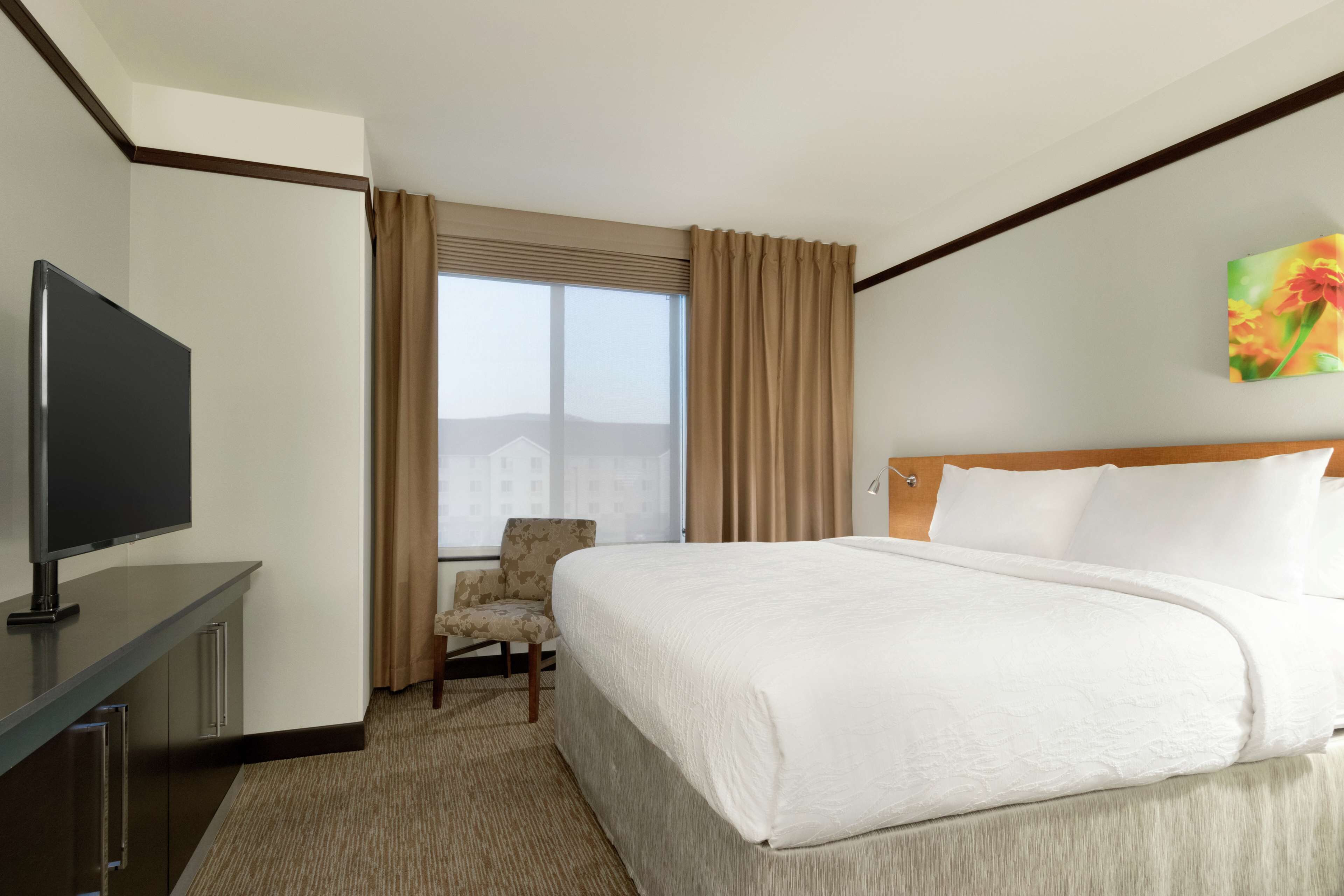 A hotel room with a bed, a TV, a chair, and a window with curtains.
