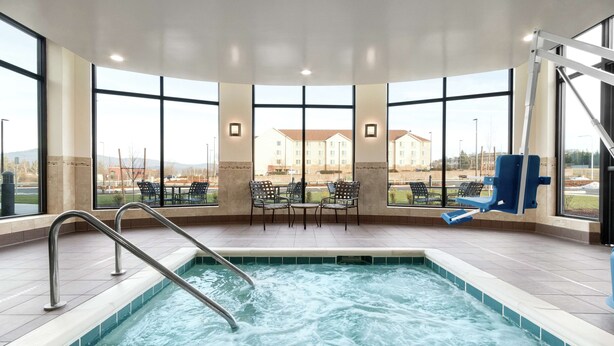 A spa area with a hot tub, seating, and large windows offering views of buildings and a distant landscape. - Hilton Garden Inn Medford, OR  (Medford)