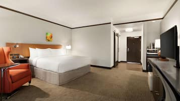 Una habitación de hotel con una cama, un escritorio con una silla, un televisor y una puerta que da a otra habitación.