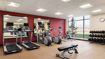A gym with treadmills, elliptical machines, a bench press, and a wall-mounted mirror.