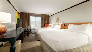 A hotel room with two beds, a desk with a lamp, a TV, and a window with curtains.