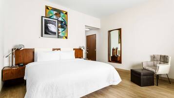 Una habitación de hotel con una cama grande, una mesita de noche de madera, una silla, un espejo y obras de arte en la pared.