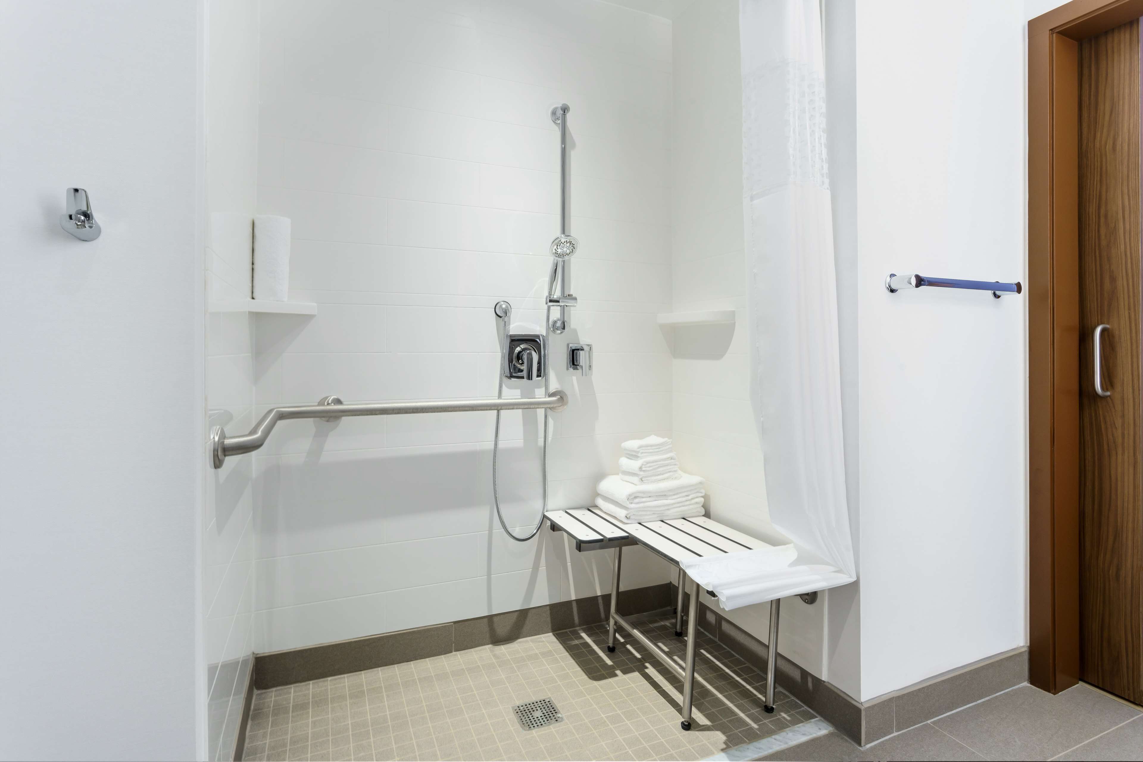 A bathroom with a shower, grab bars, a towel rack, and a wooden door.