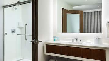 A modern bathroom with a glass shower enclosure, a white sink with a wooden vanity, and a large mirror above the vanity.