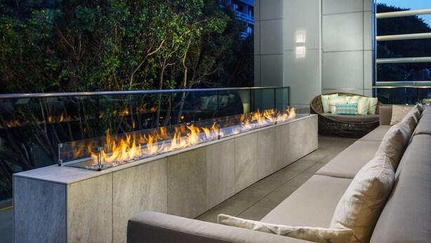 Un espace extérieur moderne, aménagé avec des sièges, un foyer intégré et une balustrade en verre.