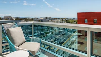 A balcony with a glass railing, a chair, and a view of the cityscape.