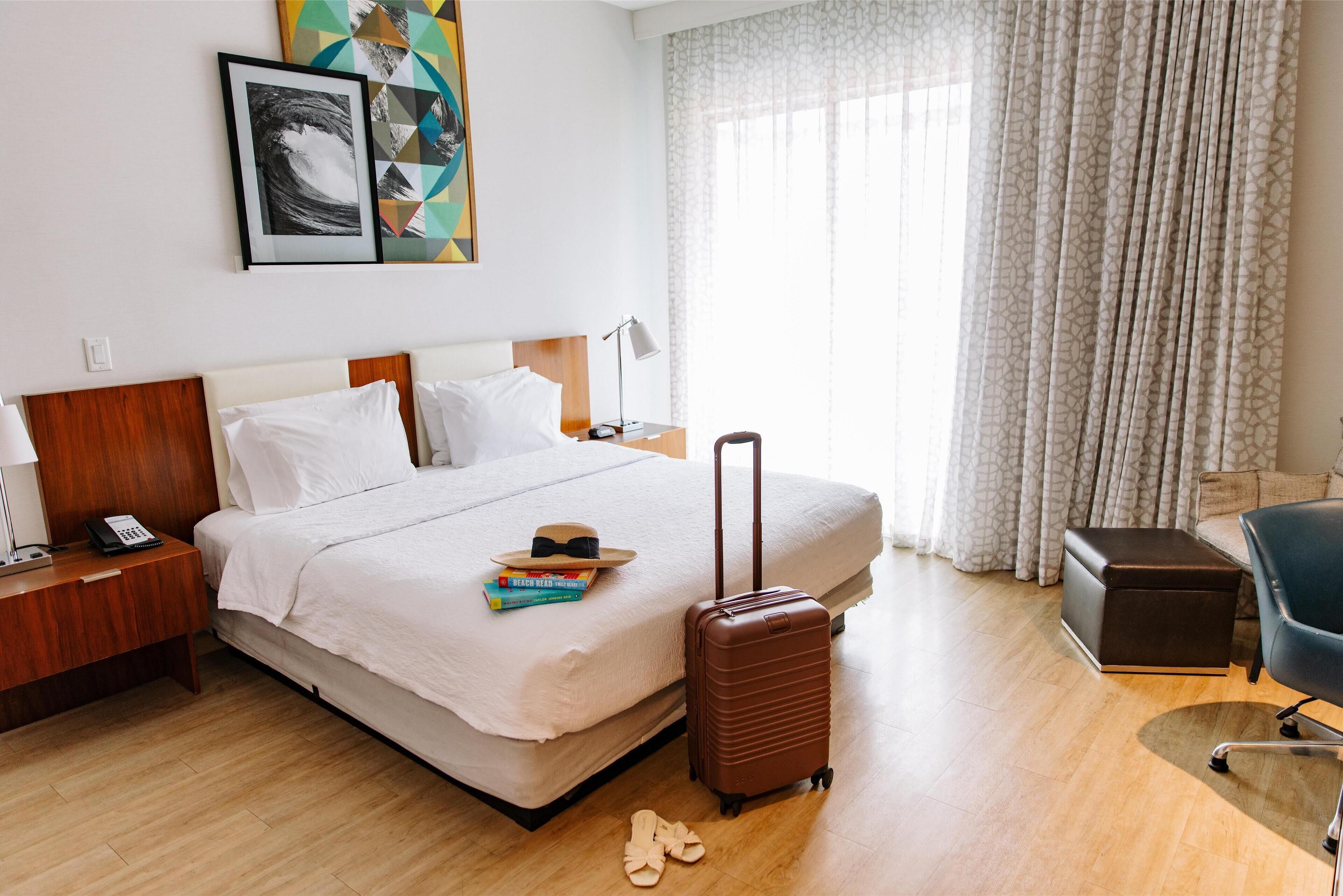 Una habitación de hotel con cama, maleta, escritorio con lámpara y una silla.