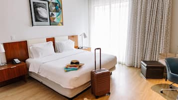 Una habitación de hotel con cama, maleta, escritorio con lámpara y una silla.