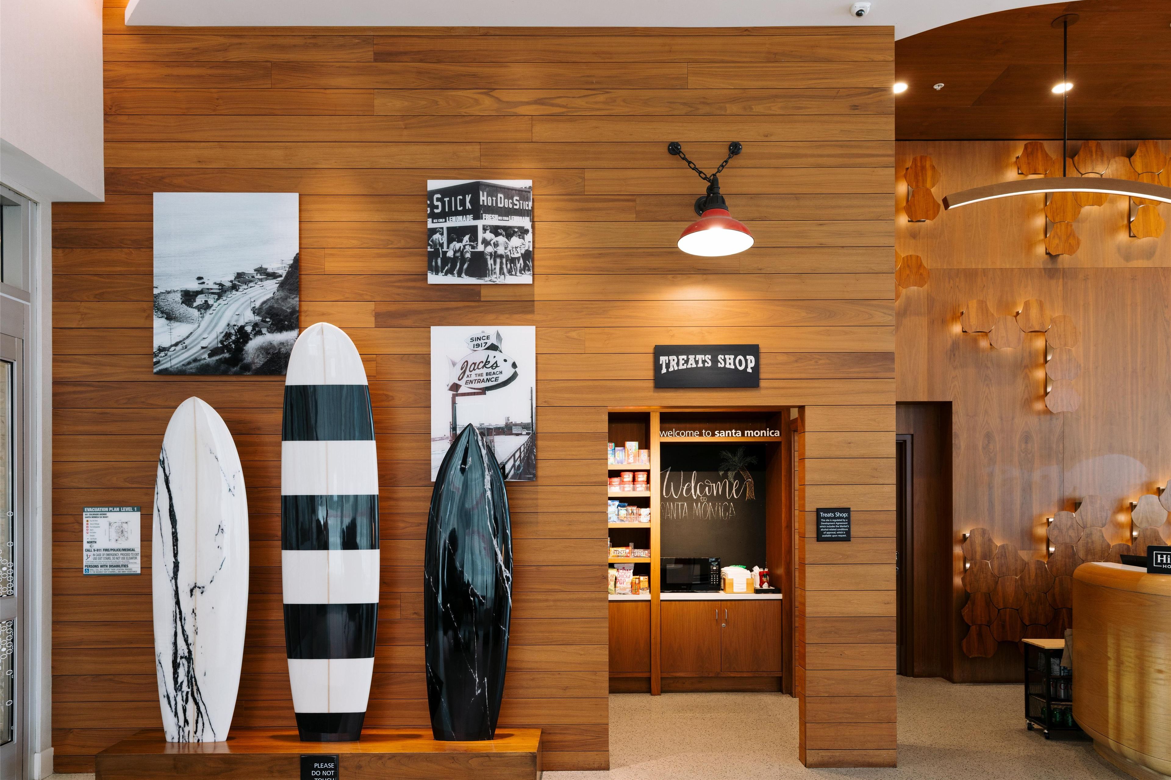 A wooden wall with surfboards, a 'TREAT SHOP' sign, and a 'Welcome to Santa Monica' sign.