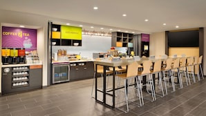 A modern coffee shop with a long counter, multiple coffee dispensers, and a seating area with chairs and tables.