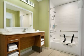 A modern bathroom with a wooden vanity, a large mirror, and a white bathtub with a showerhead.