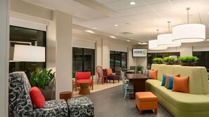 A modern office space with a green sofa, multiple chairs, a wooden table, and potted plants.