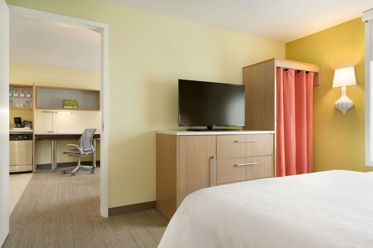 Une chambre d’hôtel comprenant un lit, un bureau avec une chaise, une télévision, une armoire et une salle de bain avec des toilettes et un lavabo.