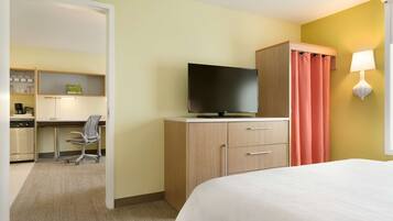 A hotel room with a bed, a desk with a chair, a television, a wardrobe, and a bathroom with a toilet and sink.
