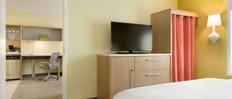 Habitación de hotel con cama, escritorio con silla, televisor, armario y baño con inodoro y lavabo.