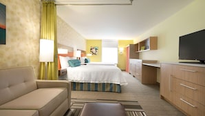 A hotel room with a bed, a sofa, a desk, a television, and a window.
