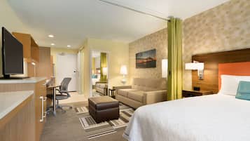 A hotel room with a bed, a desk with a computer, a sofa, a chair, and a small table with a lamp.