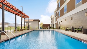 A swimming pool with a pergola, outdoor seating, and a building with large windows.