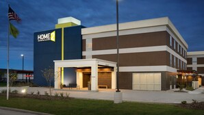 A modern hotel with a prominent 'HOME 2' sign, a covered entrance, and a well-lit exterior.