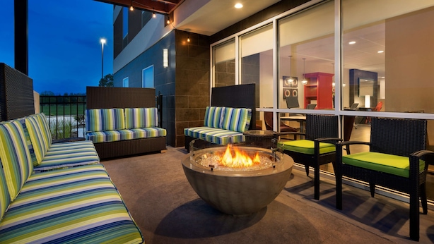 An outdoor seating area with a fire pit, cushioned sofas, and chairs with green cushions.