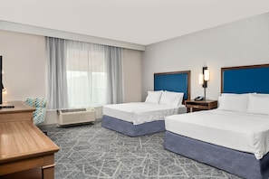 Habitació d'hotel amb dos llits, una taula de treball, una cadira, una finestra amb cortines primes i un aparell d'aire condicionat, així com un telèfon fixat a la paret.
