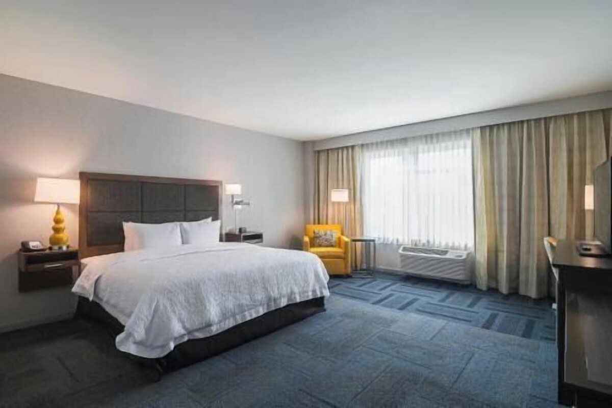 A hotel room with a large bed, a desk, a chair, and a window with curtains.