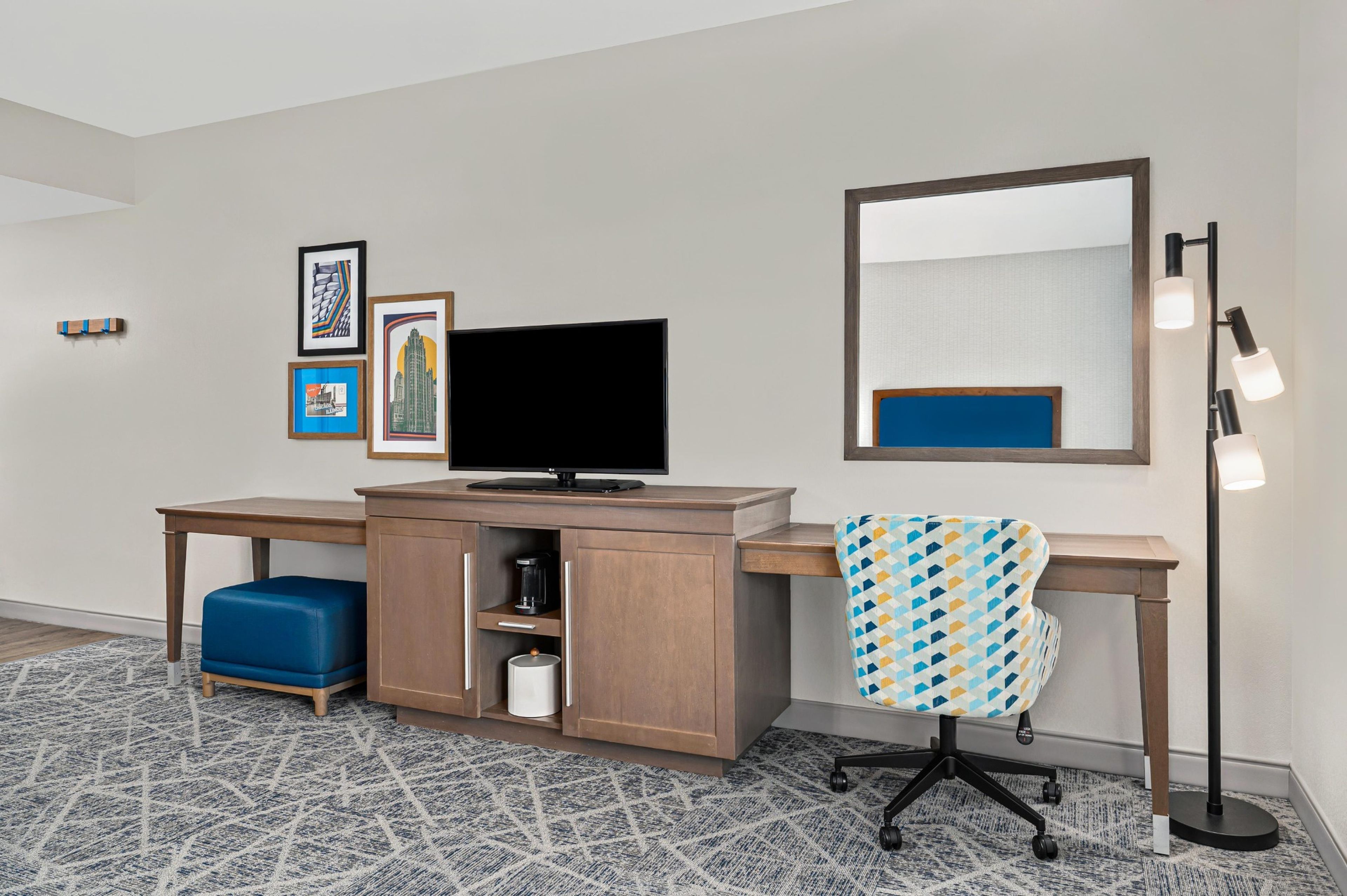 A hotel room with a desk, television, and a large mirror.