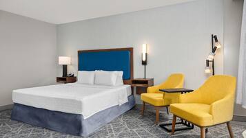 A hotel room with a large bed, a desk, a chair, and a nightstand with a lamp.