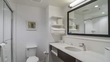 A modern bathroom with a toilet, sink, and shower. There are towels stacked on a shelf and a framed picture on the wall.
