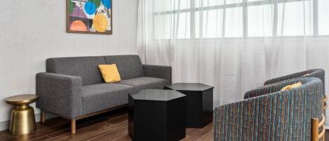 Un salon moderne avec un canapé gris, des tables d’appoint noires et des fauteuils à motifs.