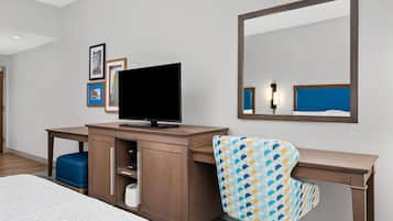 Une chambre d’hôtel comprenant un lit, un bureau avec une télévision, une chaise, une armoire et un miroir.