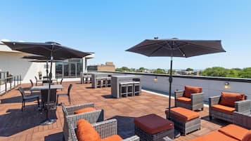 A rooftop terrace with outdoor furniture, umbrellas, and a view of the city.