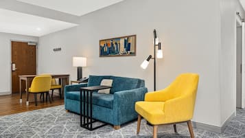 A modern hotel room with a blue sofa, yellow armchair, and a cityscape painting on the wall.
