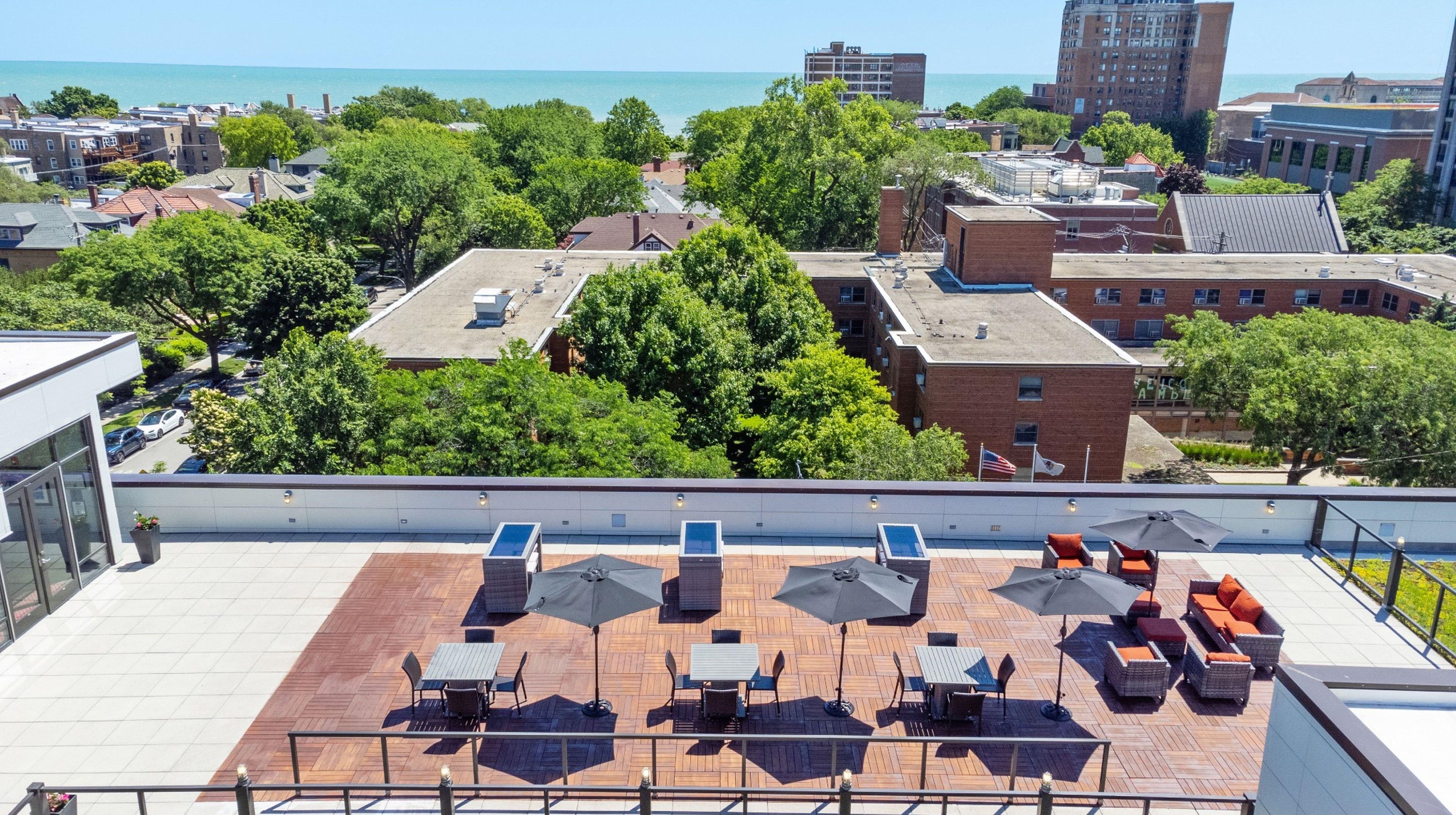 A rooftop terrace with outdoor seating, a view of the city, and a body of water in the distance.
