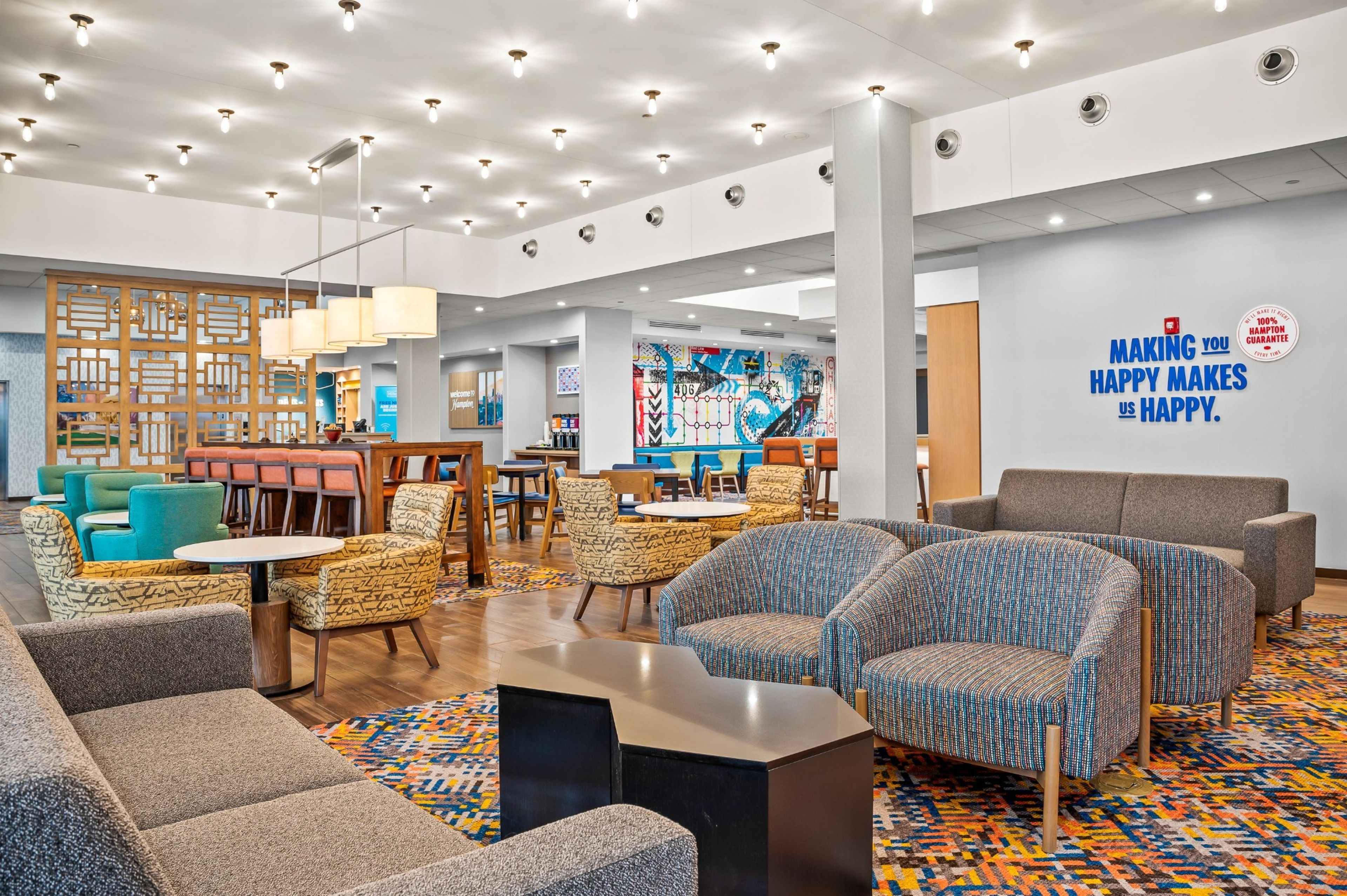 A modern hotel lobby with seating areas, a dining section, and a wall with a motivational quote.