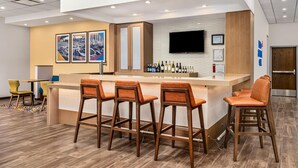 A modern bar area with wooden bar stools, a counter with a beverage display, and a mounted television. - Hampton Inn Chicago North-Loyola Station (Chicago)