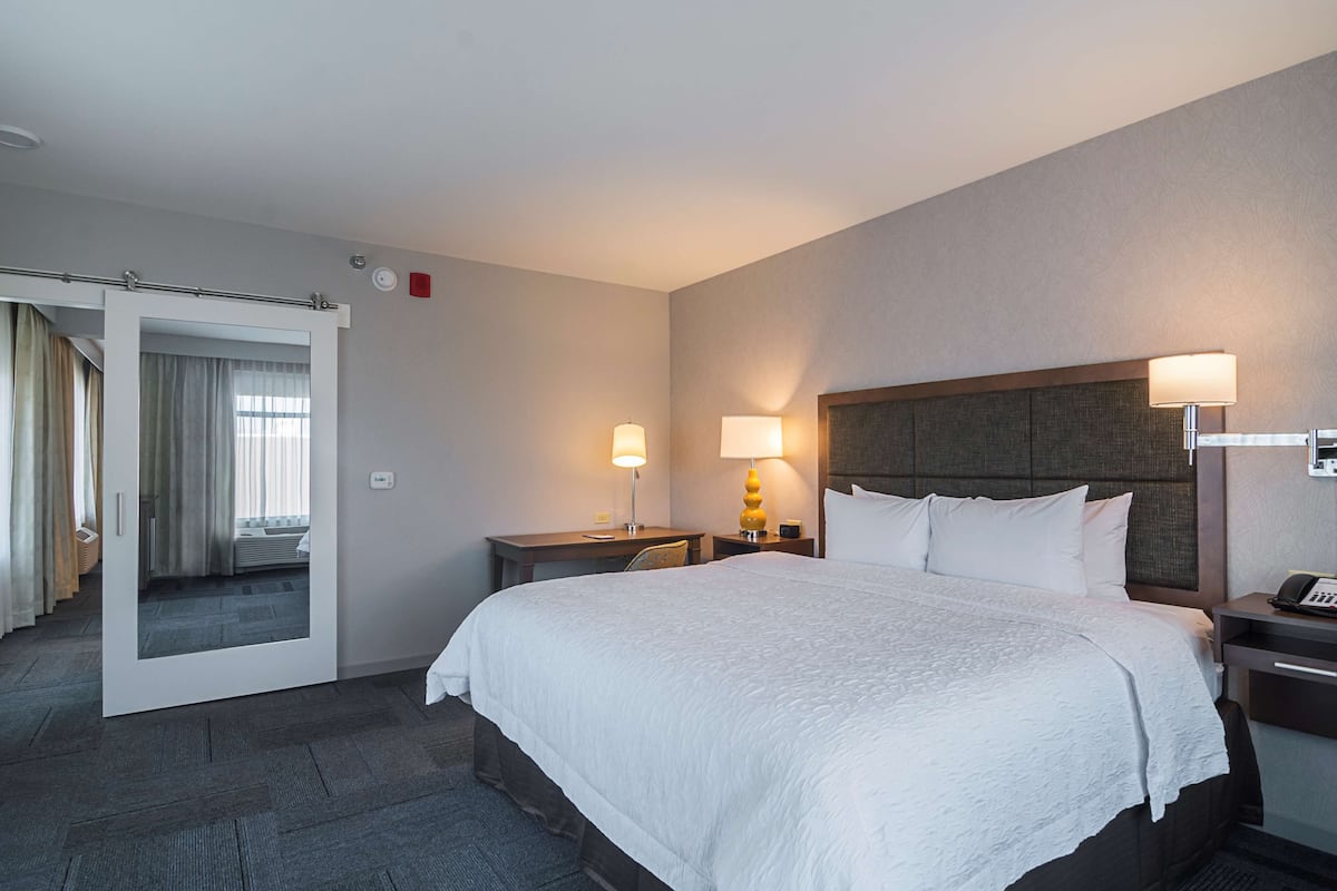 A hotel room with a large bed, bedside tables, a mirror, and a door leading to a bathroom.