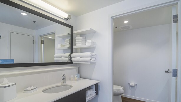 Un baño moderno con un espejo grande, lavamanos blanco y toalleros.