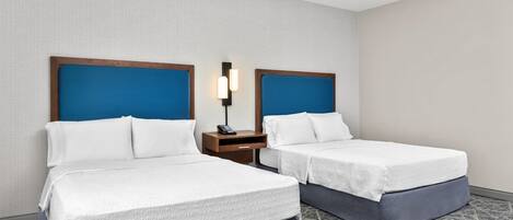 Una habitación de hotel con dos camas, una mesita de noche con lámpara y una alfombra estampada.